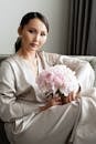 Woman in White Long Sleeve Dress Holding Pink Flower