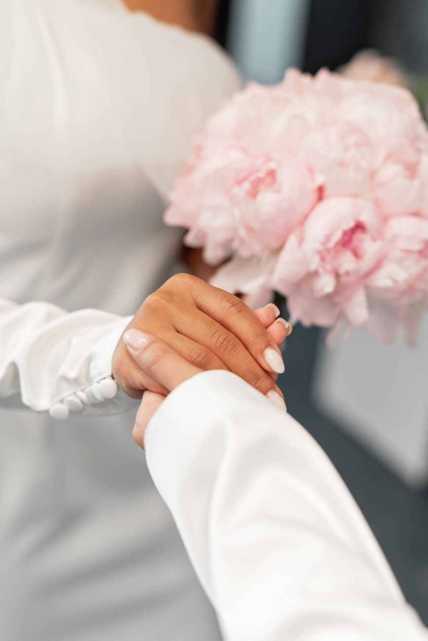Close-up of bride holding hands with a bouquet of pink peonies in wedding setting.