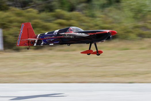 High-speed black and red model aircraft flying low over tarmac outdoors.