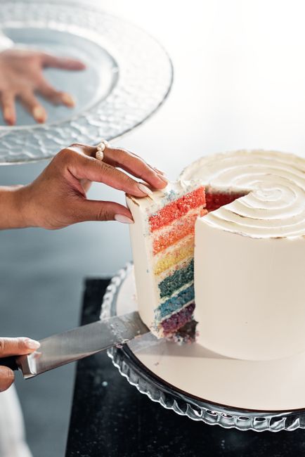 A sliced unicorn cake revealing six pastel rainbow layers, topped with a gold fondant horn, white fondant ears, and swirled pink, purple, and blue buttercream rosettes down one side.
