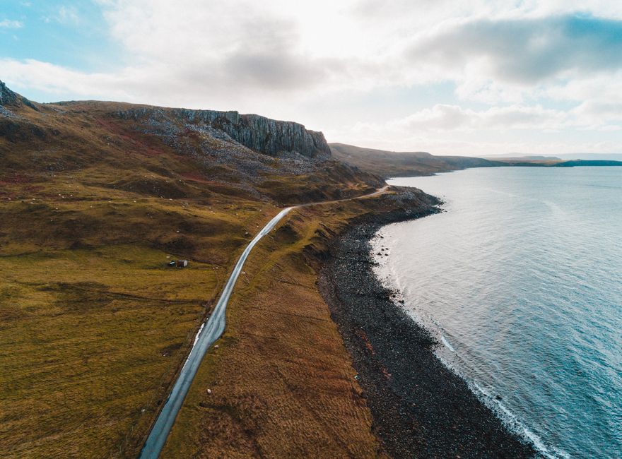 Stunning aerial view of a rugged coastline with a winding road and dramatic cliffs under a blue sky.