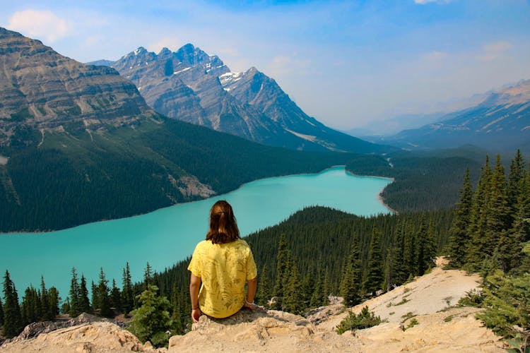 Person Sitting On Rocky Mountain Near Body Of Water