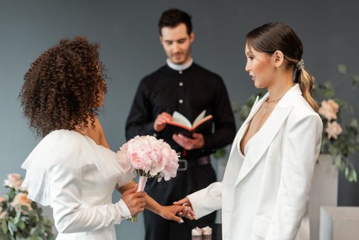 Interracial lesbian couple exchanging vows in a romantic wedding setting.