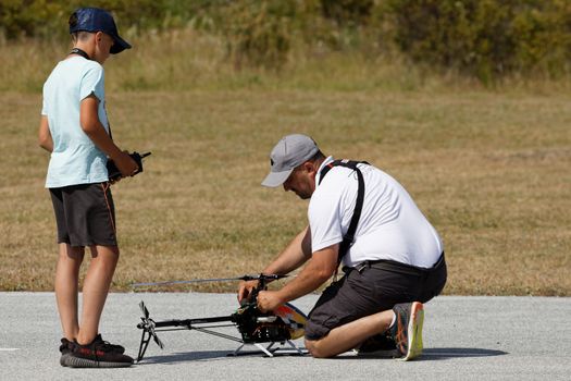 A father and son bonding over a shared hobby of flying a remote control helicopter outdoors.