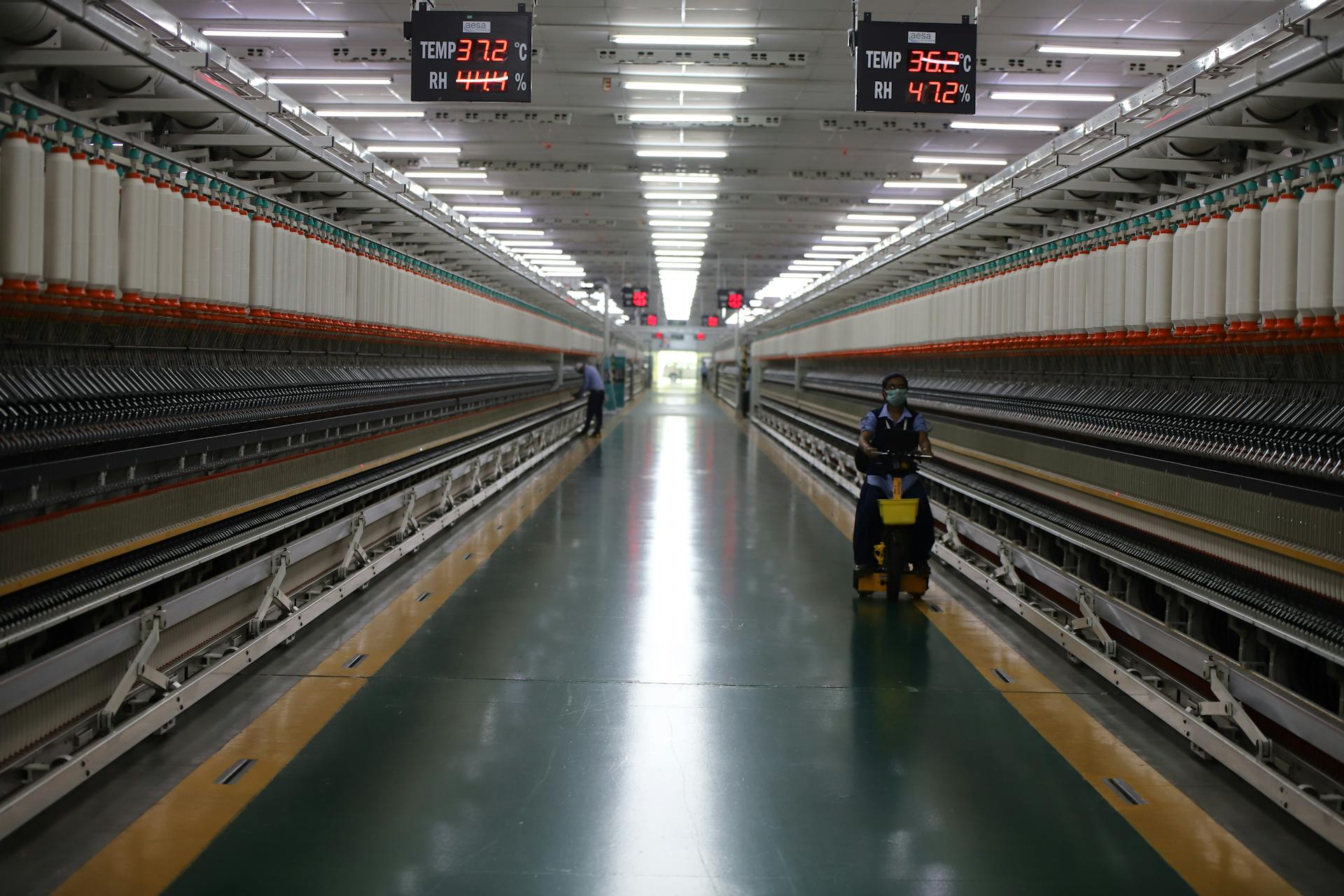 Long hallway in Indian textile factory with spinning machinery and workers.