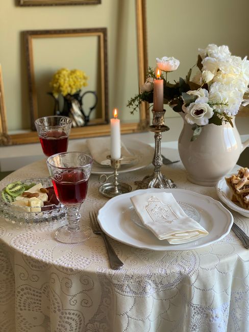 High angle of plates with food and cutlery near burning candles and white flowers placed on table with tablecloth