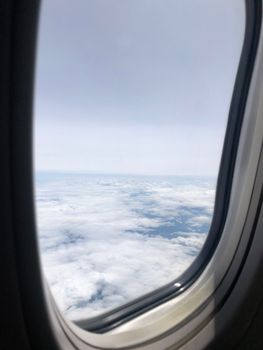 View of fluffy white clouds and blue sky from an airplane window during a daytime flight.