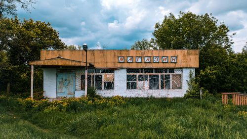 Free An abandoned rural store with overgrown grass and trees, indicative of nature reclaiming an old structure. Stock Photo