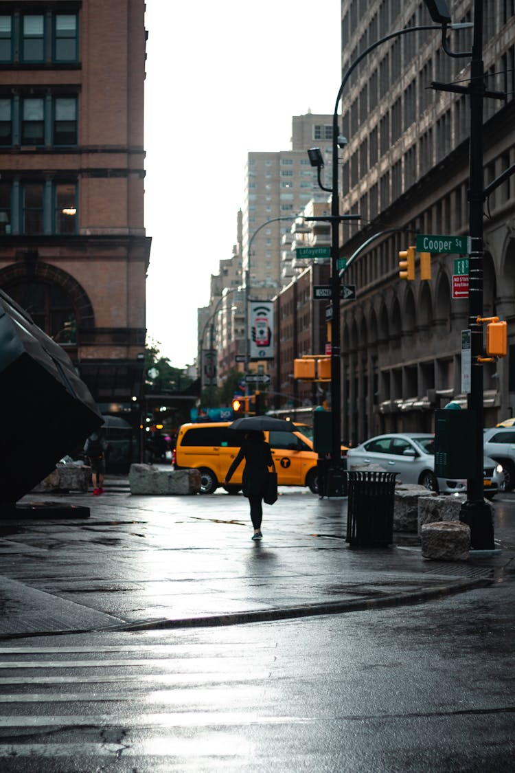 Unrecognizable Woman Crossing Street With Umbrella In Daytime