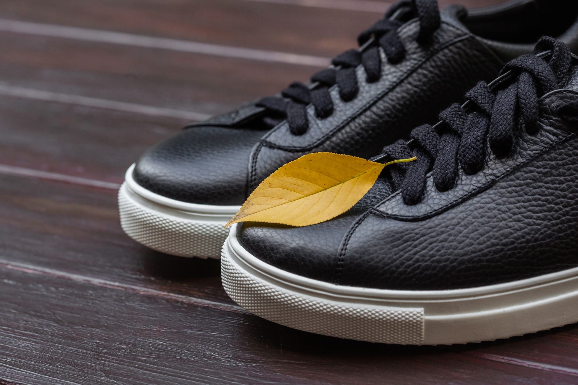 Black sneakers with a yellow leaf on wooden surface, perfect for fall fashion themes.
