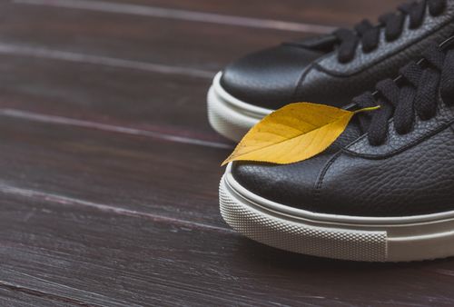 Free Stylish black sneakers with a fallen yellow leaf on wooden surface. Ideal for autumn themes. Stock Photo