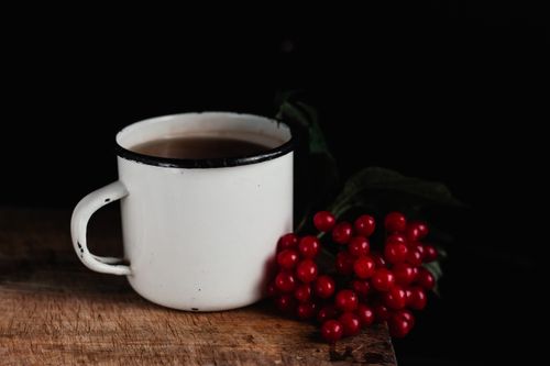 Free White enamel mug filled with coffee next to red berries on a wooden surface, against a dark background. Stock Photo
