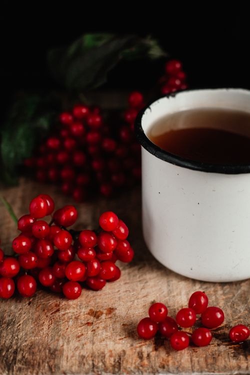 Free A rustic white cup of warm beverage beside vibrant red berries on a wooden surface. Stock Photo