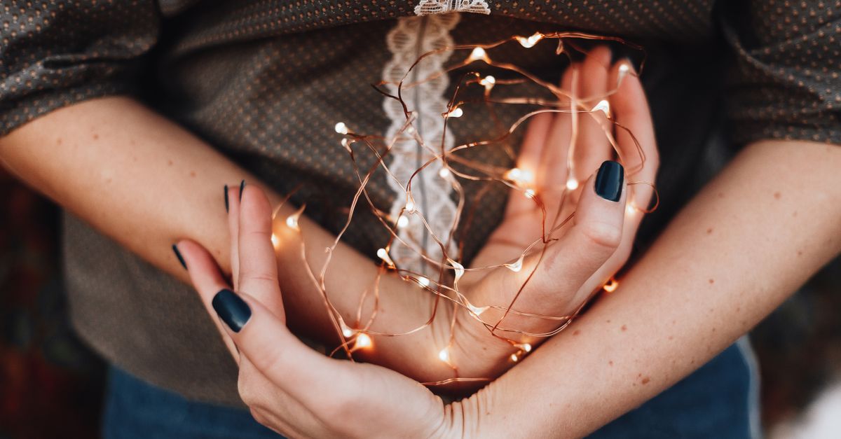 Close-up of a woman's hands gently holding glowing string lights, creating a warm festive vibe.