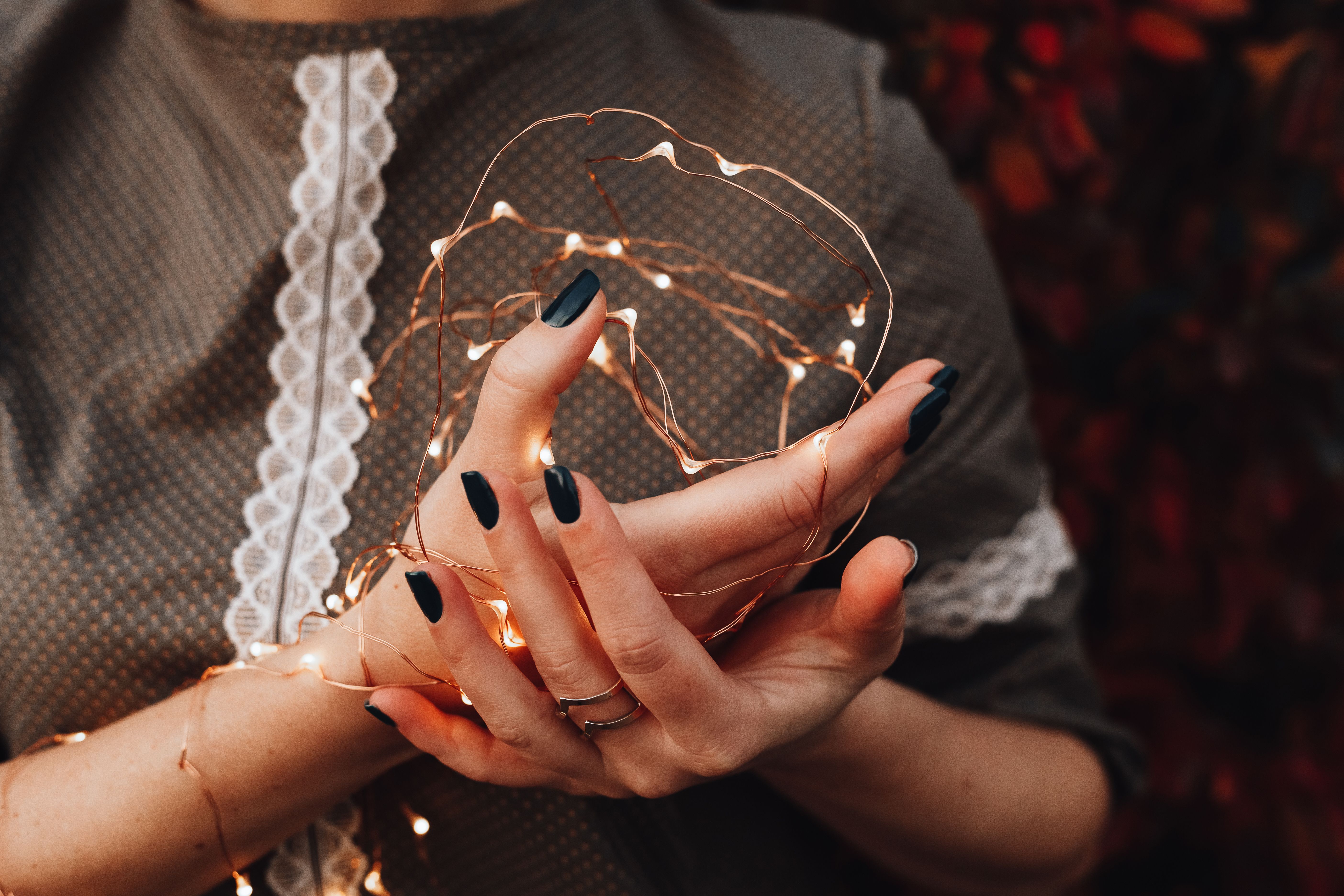 Close-up of hands with black nails holding glowing Christmas string lights in festive ambiance.