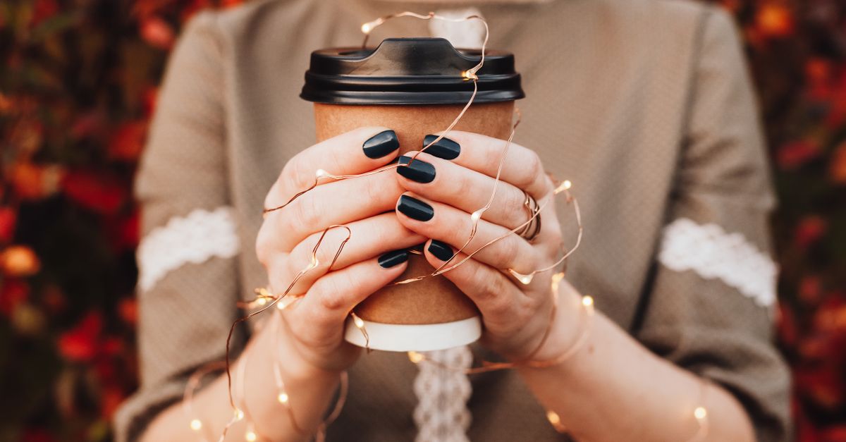 Close-up of hands holding a coffee cup with fairy lights, capturing autumn warmth.