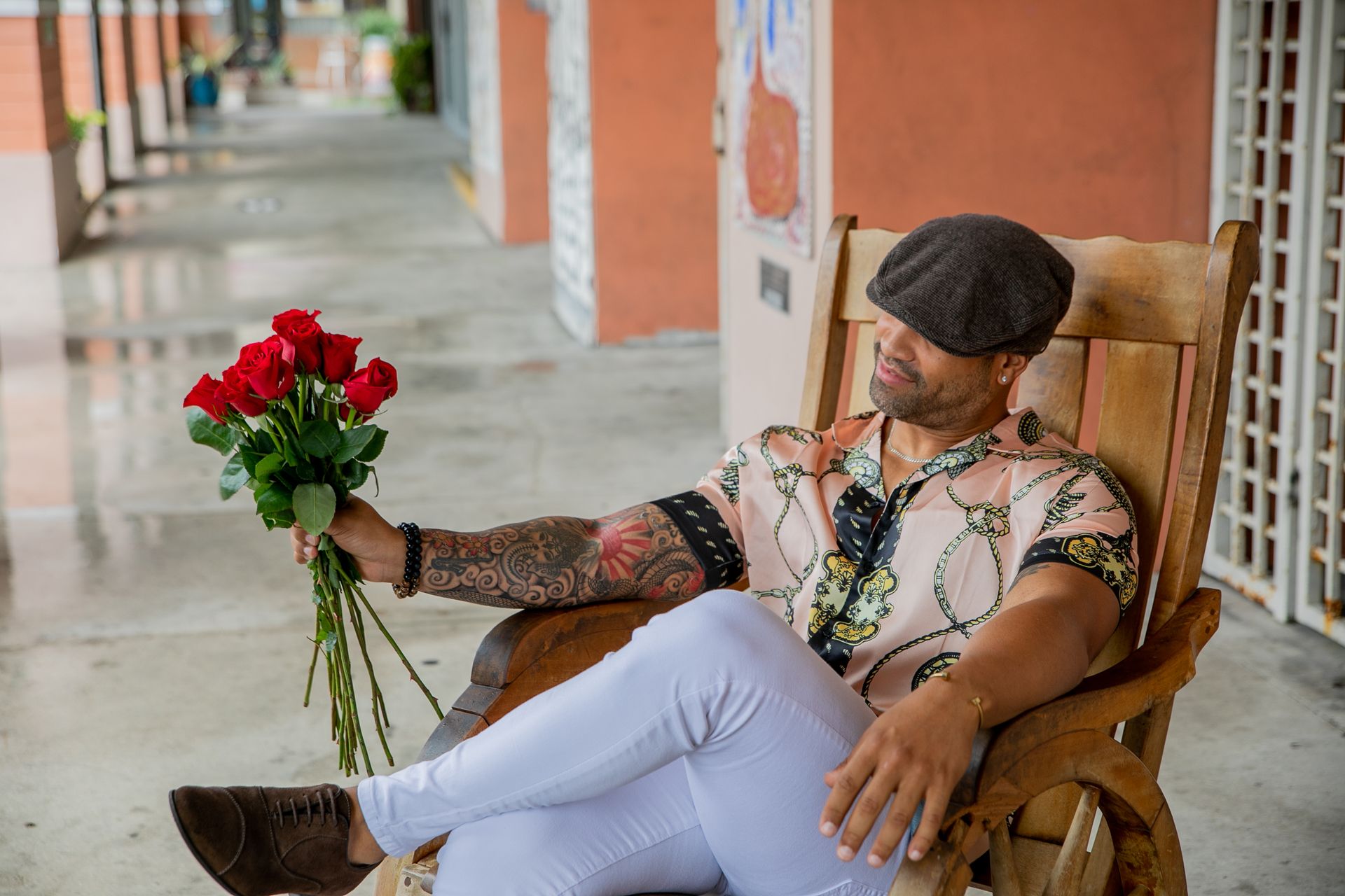 A Man with Arm Tattoo Sitting on Wooden Chair Holding a Bouquet if Red Roses