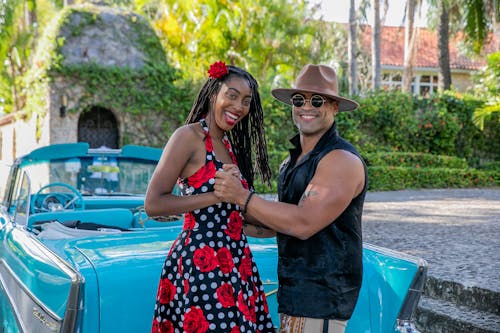 A Couple Smiling while Dancing Near a Blue Car