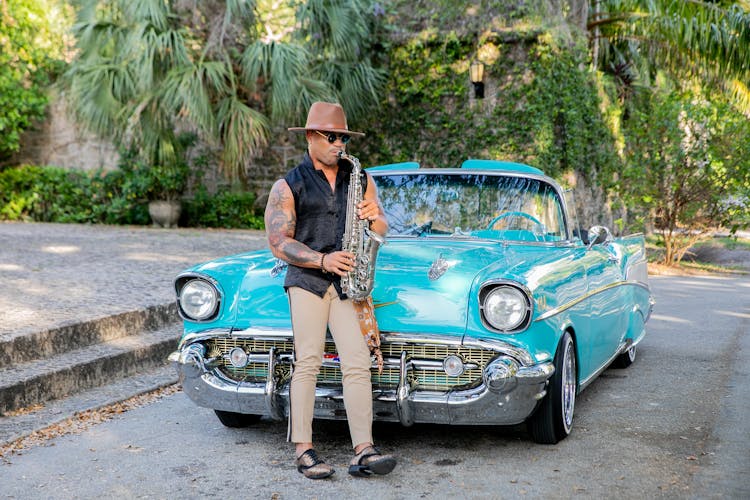 Man Playing A Saxophone Beside A Vintage Car