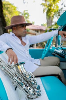 Man with hat and saxophone in a vintage car, enjoying a relaxed moment outdoors.