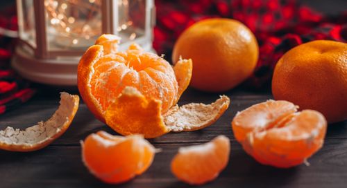 Free Vibrant peeled orange surrounded by whole citrus fruits on a wooden table. Stock Photo