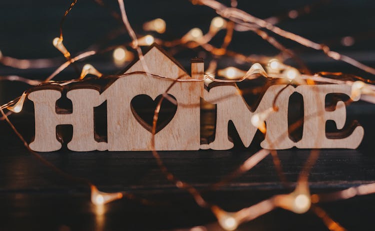 Close-up Of A Wooden Sign Home And Fairy Lights