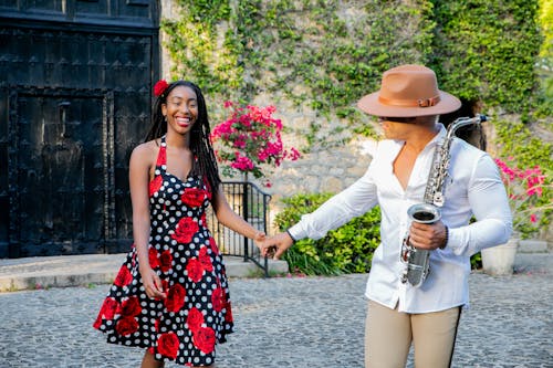 Smiling Woman in Dress Holding Hands with Man in Hat, Shirt and with Saxophone