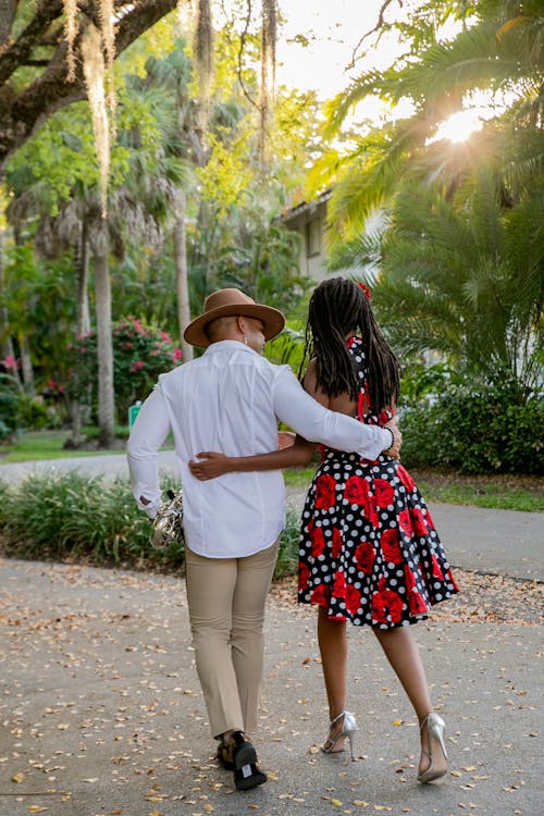 Man in Shirt and Hat Embracing and Walking with Woman in Dress