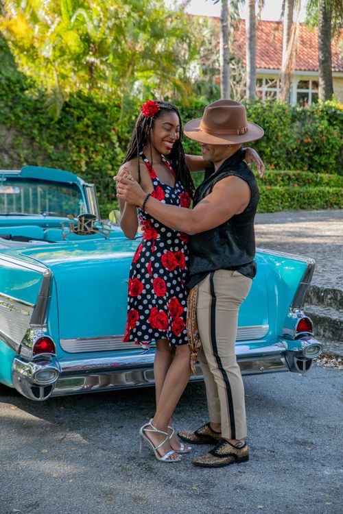 Free A joyful couple dancing near a classic blue convertible in a sunny garden setting. Stock Photo