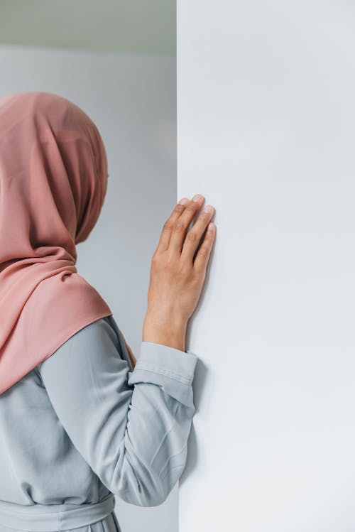 A Woman with a Hijab Touching a White Wall