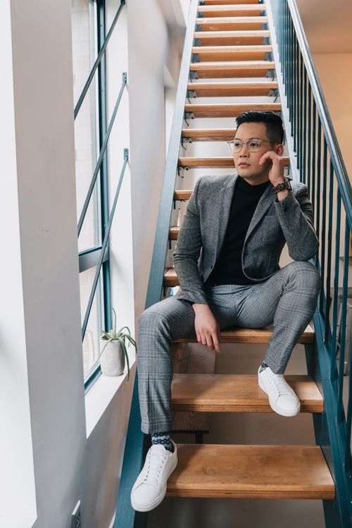 Free Stylish man in eyeglasses and plaid suit sitting on staircase indoors, showcasing modern fashion trends. Stock Photo