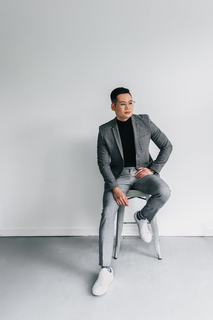 A Man In Gray Suit And Gray Pants Sitting On A Chair And Posing