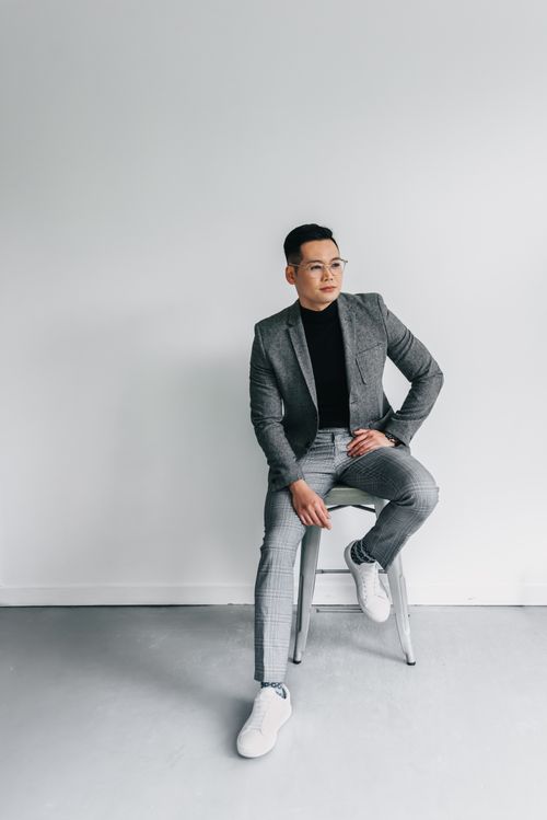 Free Fashionable man in a gray suit and white sneakers sitting in a minimalist studio setting, exuding elegance. Stock Photo