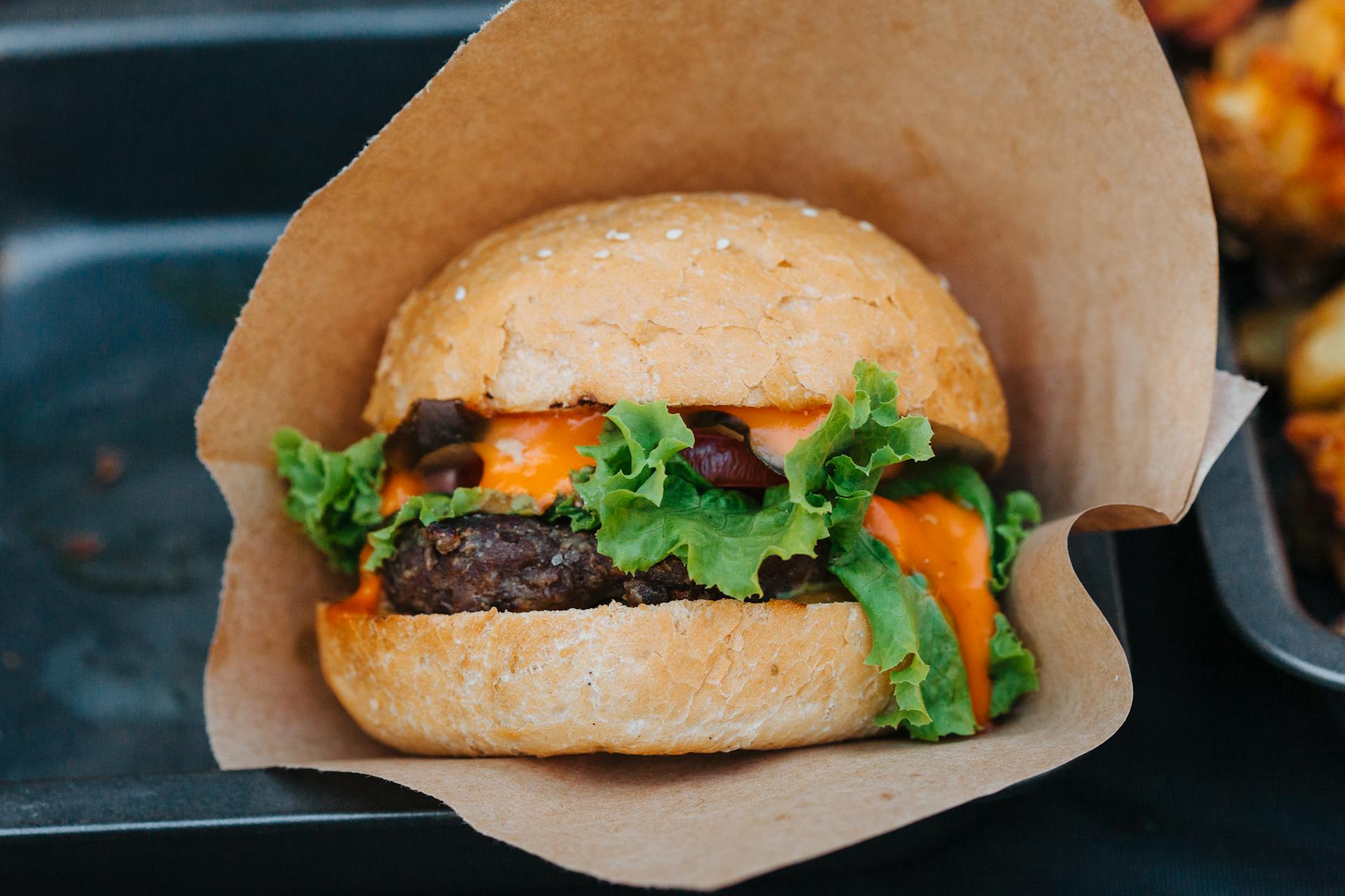 Close-up of a delicious cheeseburger with fresh lettuce and creamy sauce wrapped in paper.