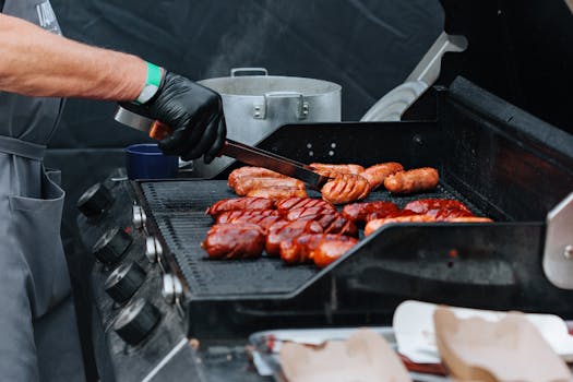 Close-up of a chef grilling various sausages on an outdoor barbecue grill, perfect for summer events.