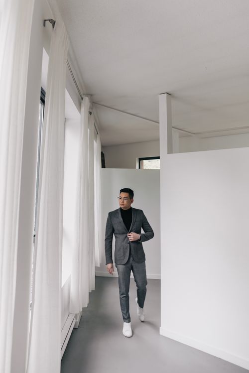 Free Elegant man in a gray suit walking through a minimalist white hallway. Modern and sophisticated atmosphere. Stock Photo