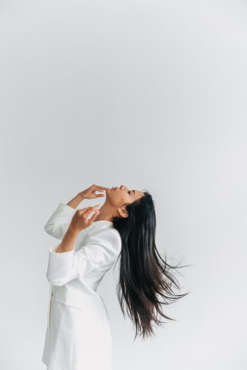 Free Portrait of a woman in a white suit leaning back with flowing hair against a clean background. Stock Photo