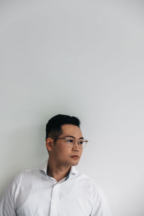 Free A thoughtful East Asian man wearing glasses and a white shirt against a neutral background. Stock Photo