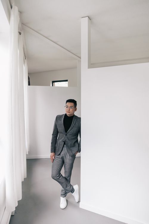 Free Asian man in a sleek gray suit posing confidently in a minimalistic office space. Stock Photo