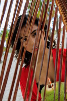 Woman in red enjoying a tropical scene through palm fronds with a coconut drink.