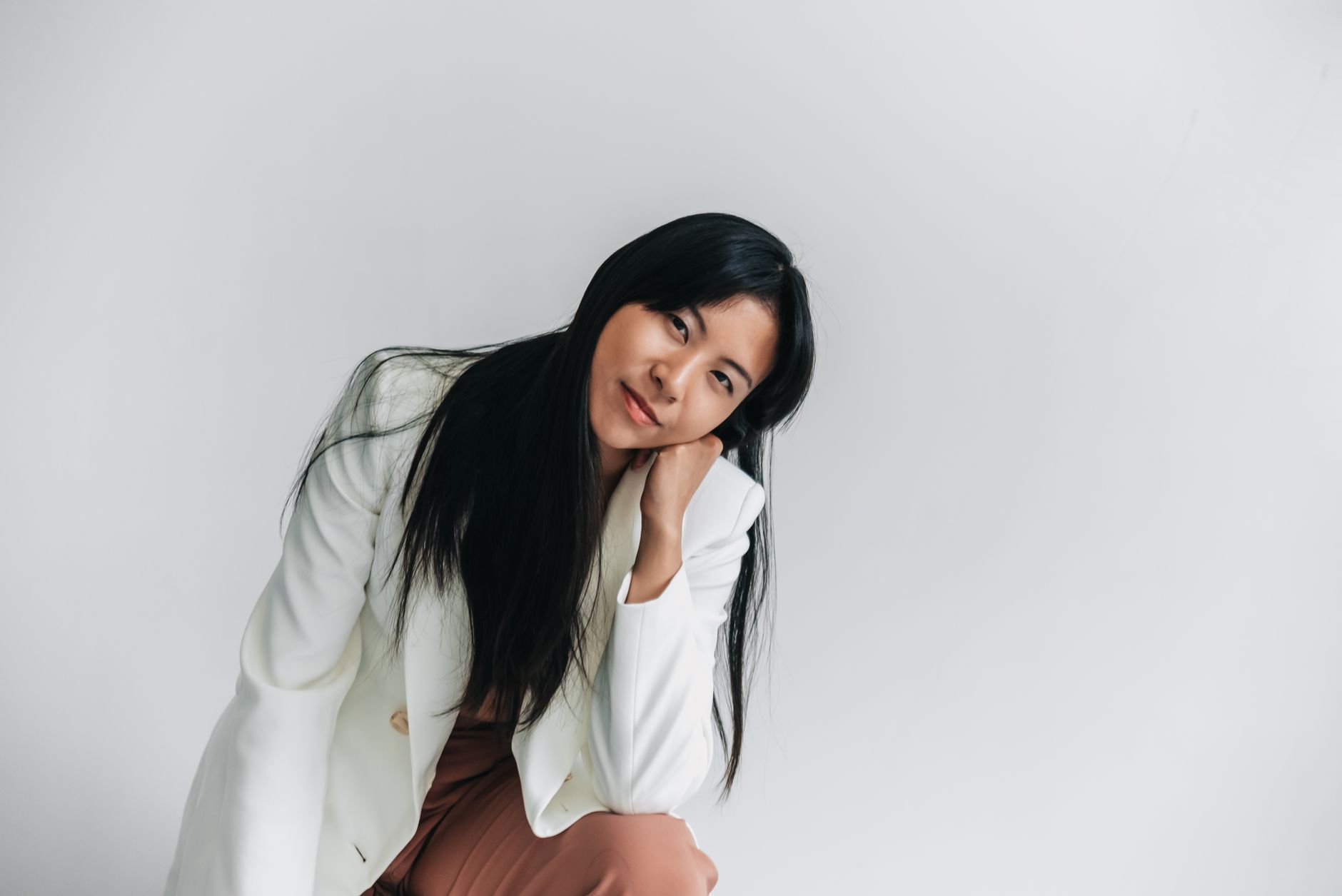 Portrait of an elegant woman posing with hand under chin, smiling against a minimalist white backdro