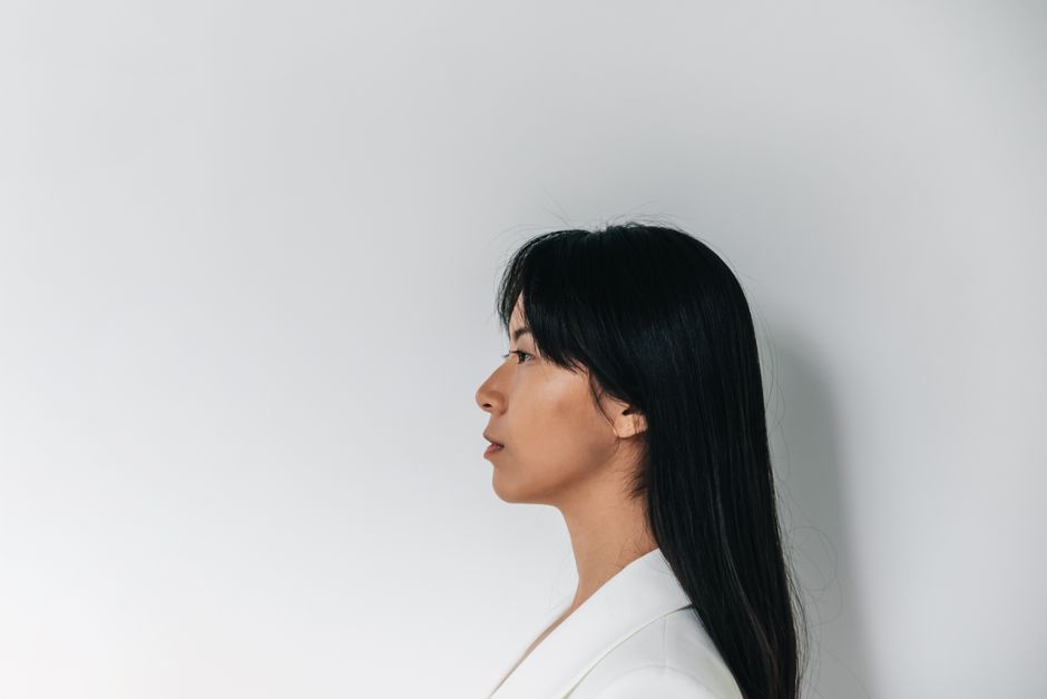 Profile view of an Asian woman standing against a plain white background in a minimalist style.
