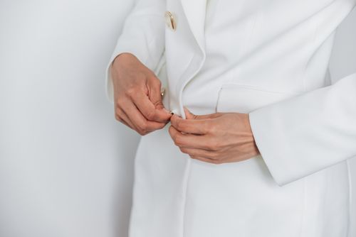 Free Close-up of adult hands buttoning a white coat, showcasing elegance and style. Stock Photo