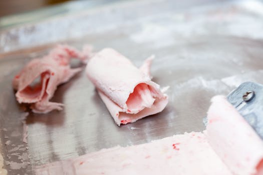 Delicious pink rolled ice cream in the making on a cold pan, a trendy frozen dessert.