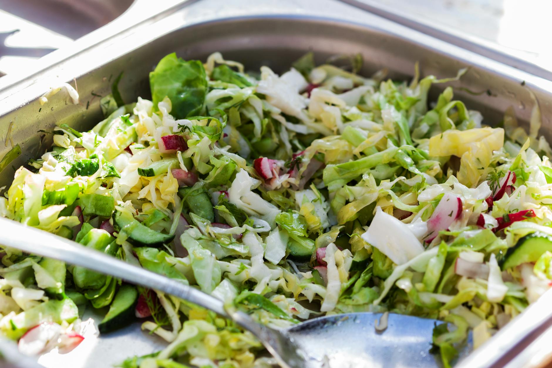 Close-up of fresh vegetable salad with cucumbers, cabbage, and radishes, served in a stainless steel tray.
