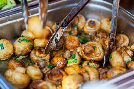 Golden sauteed whole button mushrooms with sliced scallions in a steel pan with tongs