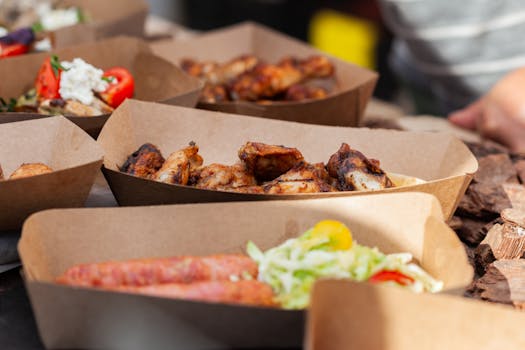 Close-up of assorted street food in eco-friendly trays, showcasing meat and salads.