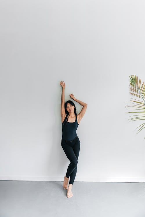 Woman in a Black Tank Top Posing on a White Wall
