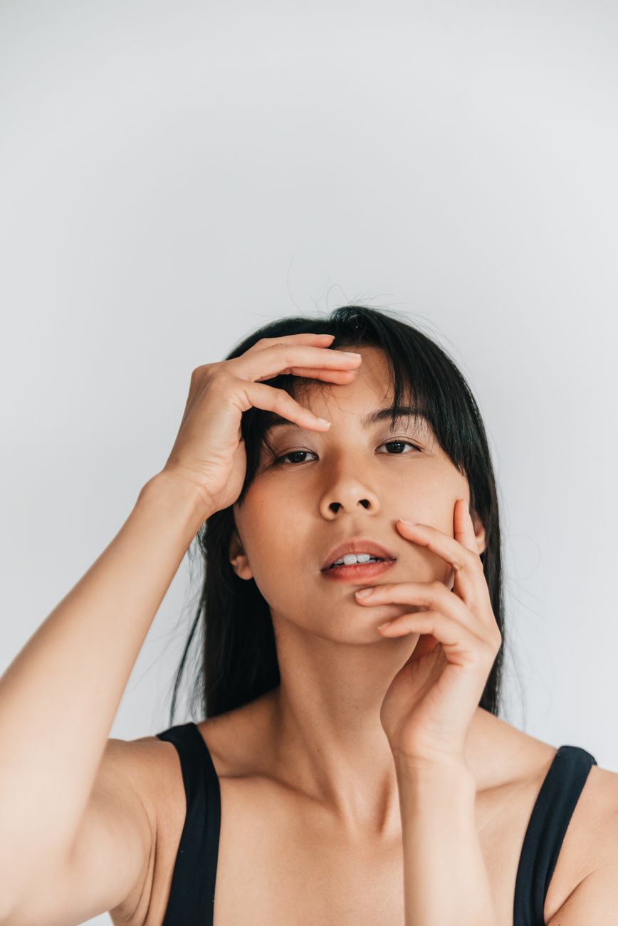A stunning minimalist portrait of a woman posing with hands on her face in a studio setting.