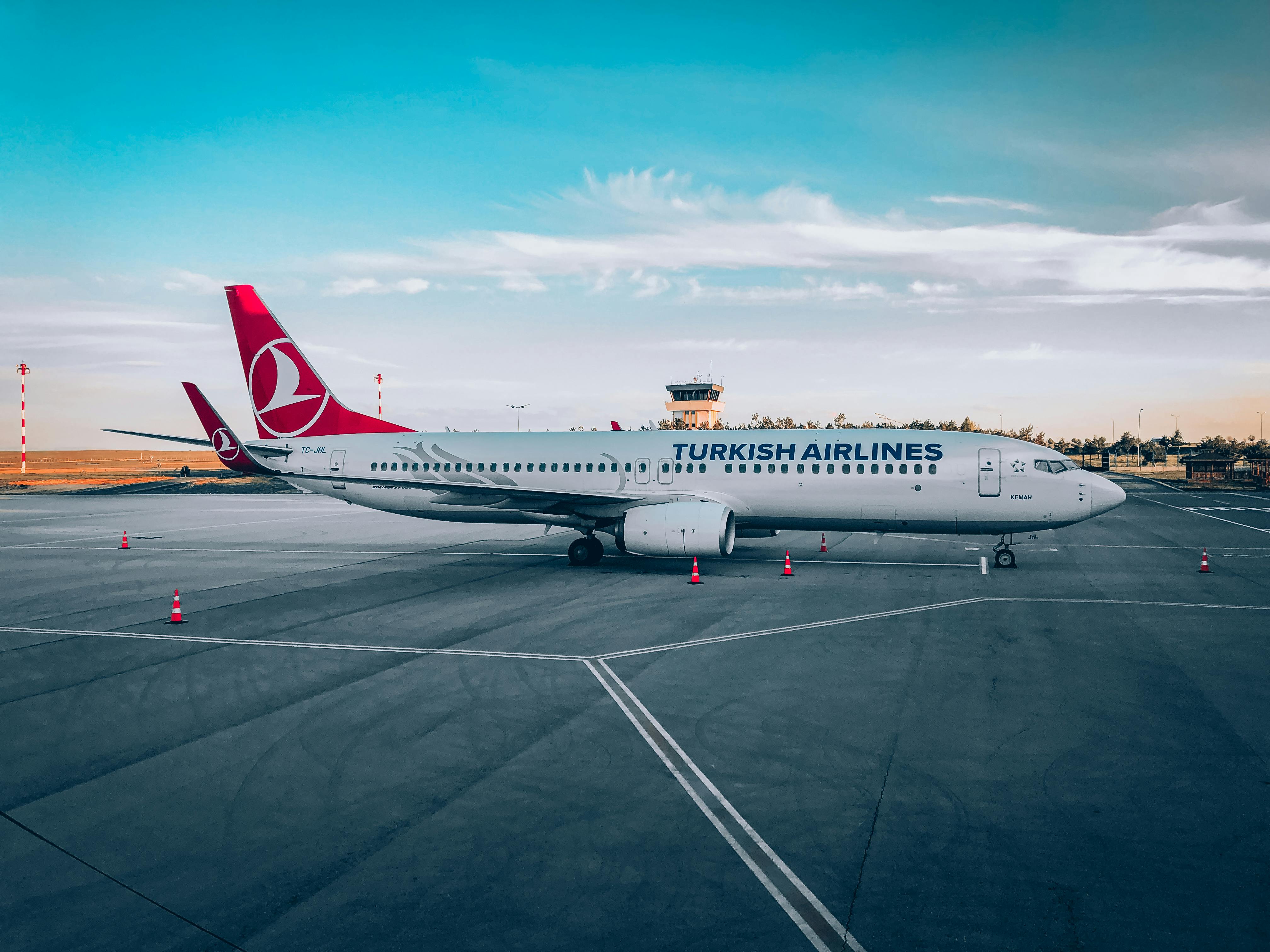 Free Turkish Airlines aircraft parked at the airport runway under a cloudy blue sky, early morning scene. Stock Photo
